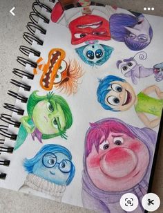 a spiral notebook with cartoon characters drawn on it and colored pencils in the background