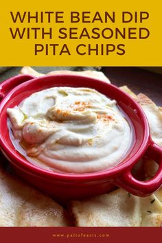 white bean dip with seasoned pita chips in a red bowl on a wooden table