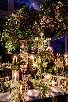 an image of a table setting with candles and flowers in the center, surrounded by greenery