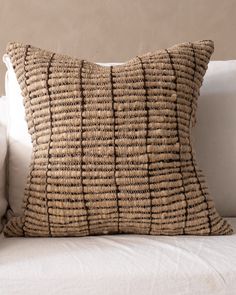 a close up of a pillow on a couch with a white pillow and beige wall in the background