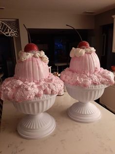 two large cakes sitting on top of white pedestals covered in pink frosting and topped with cherries