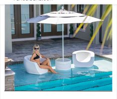 a woman sitting in a chair next to a pool with an umbrella over her head