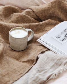 a cup of coffee sitting on top of a bed next to an open book and magazine