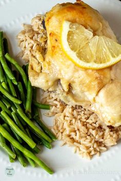 a white plate topped with chicken, rice and asparagus next to lemon wedges