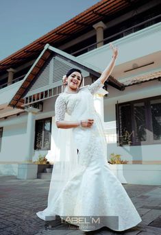 a woman in a white wedding dress standing on a brick floor with her arms up