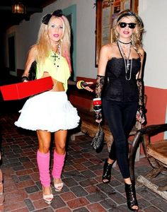 two women dressed in costumes walking down the street with one holding a red skateboard