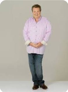 a man standing in front of a white background wearing a pink shirt and blue jeans