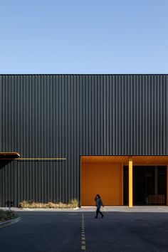 a person walking down the street in front of a black building with yellow doors and windows