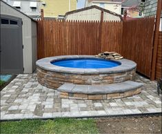 a small backyard with a stone fire pit and brick pavers around the hot tub