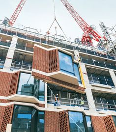 two cranes are on the side of a tall building with red bricks and glass windows