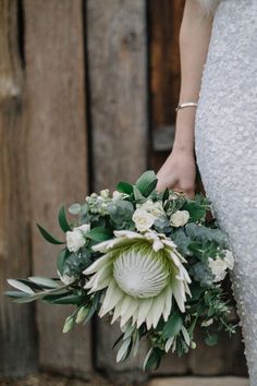 a bride holding a bouquet of flowers in her hand and standing next to a wooden wall