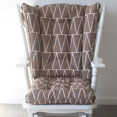 a white rocking chair with brown and white patterned seat cover on it's back