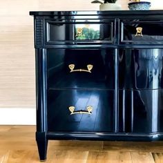 a black dresser with gold handles and knobs on the doors is in front of a white wall