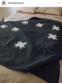 a black blanket with white stars on it sitting on top of a bed next to pillows