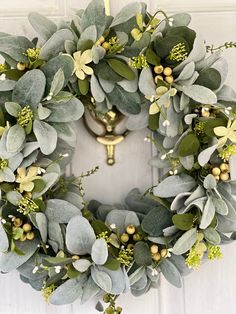 a wreath hanging on the front door with green leaves and greenery around it's edges