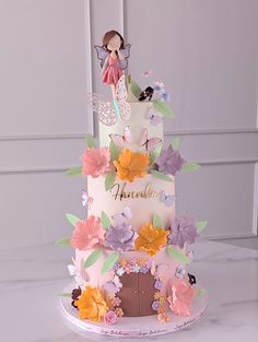 a three tiered cake decorated with flowers and a fairy figurine on top