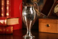 a silver trophy sitting on top of a wooden table next to books and a clock