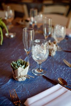 the table is set with wine glasses, silverware and succulents on it