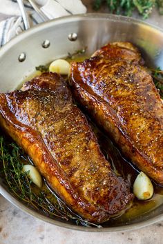 two pieces of meat in a pan with herbs