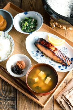 a wooden tray topped with bowls and plates filled with different types of food on top of it