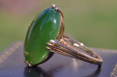 The Penbrook Vintage Signed Jade Ring in Yellow Gold. The center is set with a oval shaped cabochon natural nephrite jade of a lovely green color with measurements of 20mm x 14.7mm x 3.9mm. The ring features four sets of three prongs located at the north south east and west directions. The ring is crafted in yellow gold and is very comfortable to wear. The ring has a nice presence on the hand yet sits low! The ring is a finger size 8.25 and is able to be resized for an additional charge. Each pi Formal Oval Jade Emerald Ring, Classic Green Cabochon Ring, Green Oval Cabochon Emerald Ring For Wedding, Green Emerald Oval Cabochon Ring For Wedding, Formal Green Cabochon Emerald Ring, Elegant Domed Emerald Ring, Oval Jade Rings Hallmarked, Elegant Green Domed Jewelry, Art Deco Round Green Emerald Ring