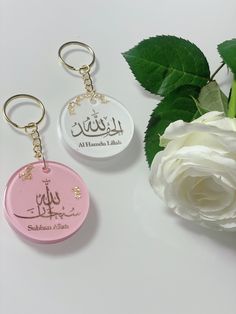 two key chains with arabic writing on them next to a white rose