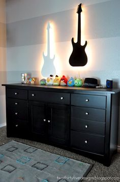 a room with a black dresser and guitars on the wall above it, along with a gray rug