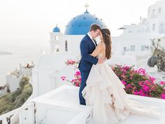 a bride and groom standing on the roof of a building with flowers in front of them