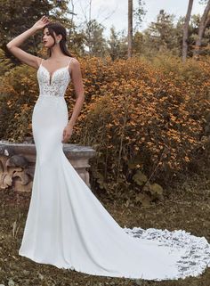 a woman in a white wedding dress standing on a stone bench with her arms behind her head