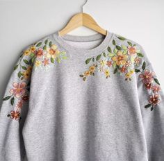 a gray sweater with flowers on it hanging from a wooden hanger next to a white wall