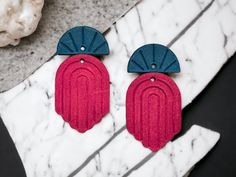 pair of red and blue earrings with fan shaped design on marble surface next to doughnut