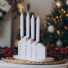 a white candle holder with four candles on top of it next to a christmas tree