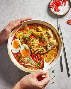 two hands holding a bowl of ramen with an egg on top