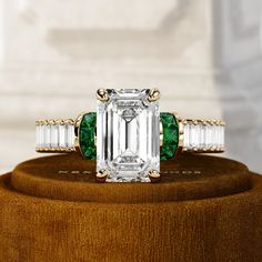 an emerald and white diamond ring on top of a wooden stand in front of a marble wall