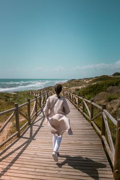 a woman walking down a wooden walkway next to the ocean