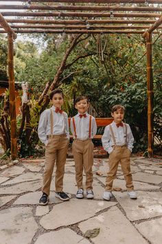 three young boys wearing suspenders and bow ties standing in front of a pergolan