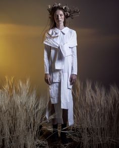 a woman standing in a field wearing a white coat and wreathed headdress