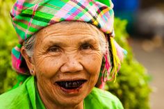 an old woman wearing a green shirt and colorful head scarf smiling at the camera with her mouth open