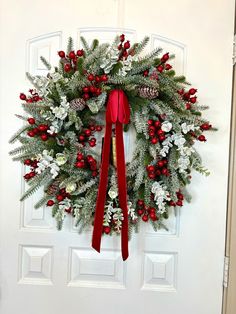 a christmas wreath hanging on the front door with red ribbon and pineconis, berries, and evergreen cones