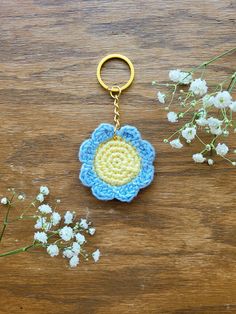 a crocheted flower keychain sitting on top of a wooden table next to flowers