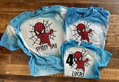 two shirts with spiderman on them sitting on a wooden floor next to each other