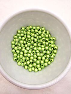 a white bowl filled with lots of green beads