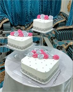 three white cakes with pink roses on top sitting on a table in front of blue curtains