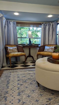 a living room with two chairs and a table in front of a window that has curtains on the windowsill