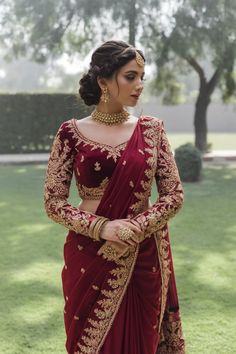 A photo of a Pakistani bride wearing a rich red bridal saree with intricate golden embroidery along the borders. The saree is paired with a matching blouse that has bold golden motifs on the sleeves and neckline. Designer Bridal Sarees Wedding, Bengali Bride Outfits, Red Indian Bridal Outfit, North Indian Wedding Outfits, Red Wedding Sarees, Red Wedding Sarees For Bride, Red Embroidery Saree, Royal Indian Bride Outfit, Minimalist Indian Bride