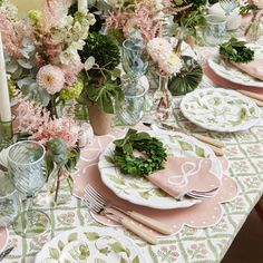 the table is set with pink and white plates, silverware, and greenery