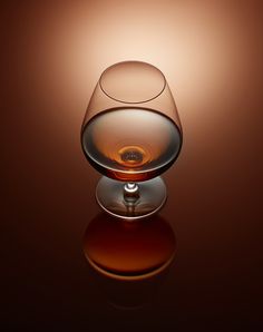 an empty wine glass sitting on top of a reflective surface in front of a brown background