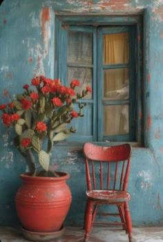 a red chair sitting in front of a window next to a potted plant on top of a table