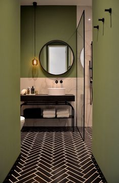 a bathroom with a black and white checkered floor, green walls and a round mirror on the wall