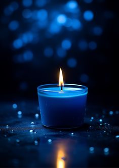 a blue candle is lit on a dark surface with water droplets around it and the light shining brightly